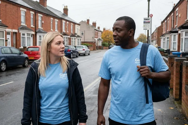 Two Giant Healthcare support workers in light blue branded T-shirts walking along a residential street mid conversation