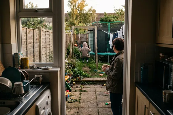 A child on a garden swing seen from behind at a distance while a parent watches from the patio