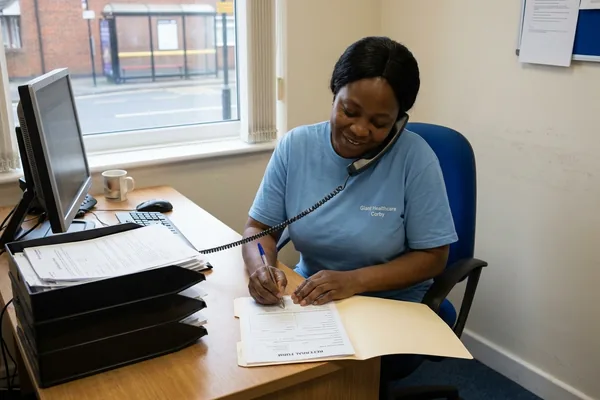 A registered manager at an office desk taking referral notes during a phone call